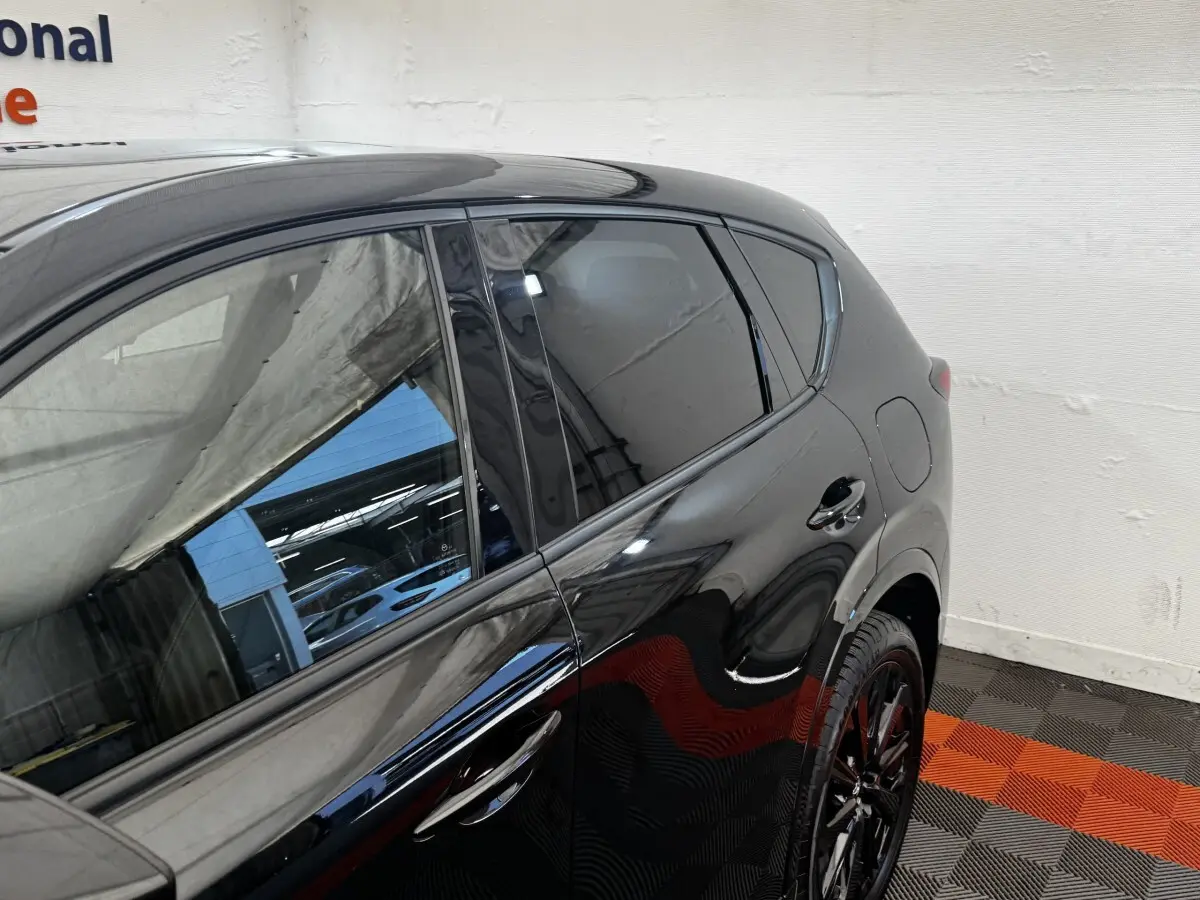 Vue latérale droite du Mazda CX-60 noir 2024 avec jantes noires et vitres teintées dans un garage.