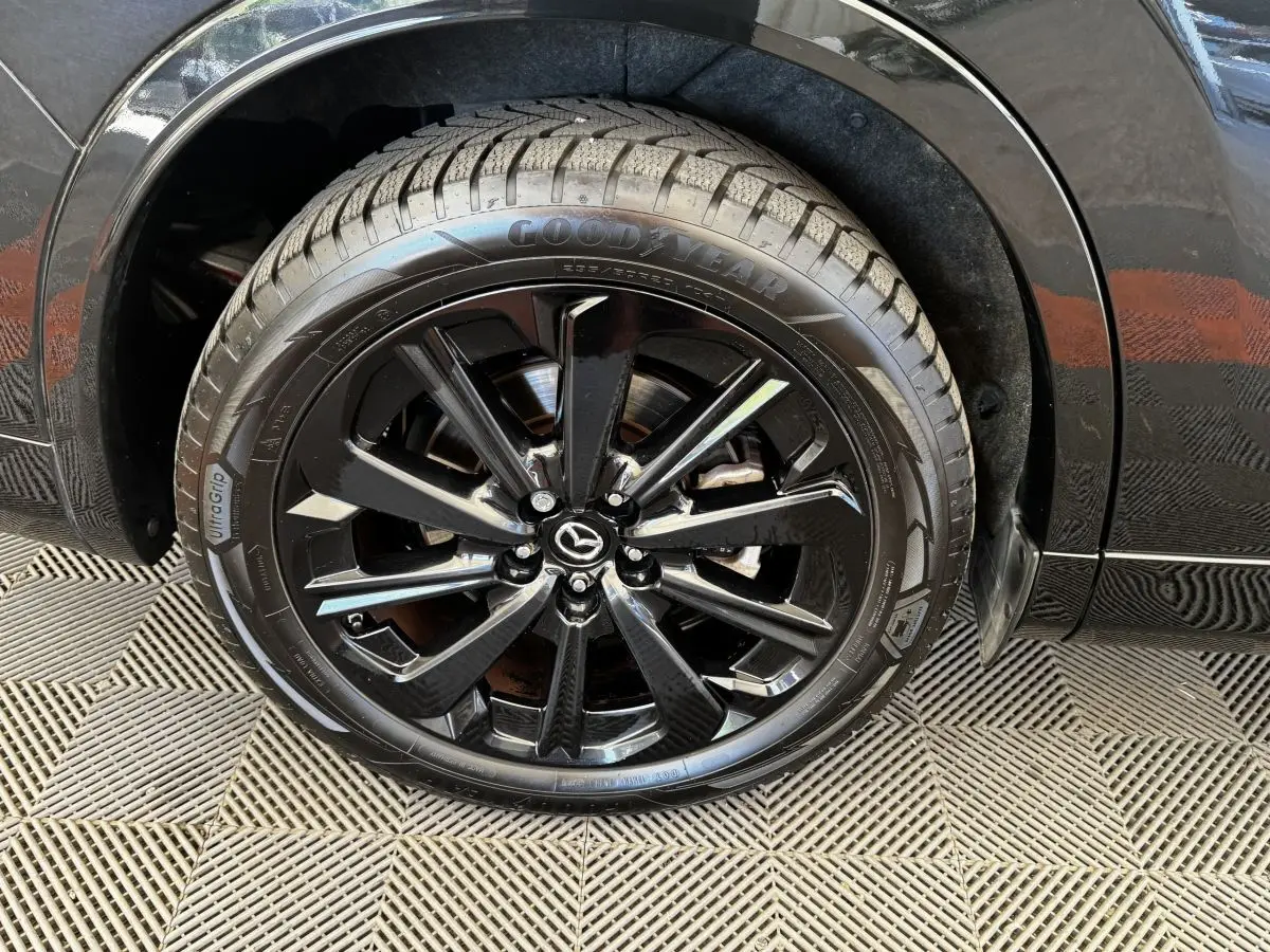 Gros plan sur la roue avant droite noire brillante du Mazda CX-60 2.5 e-Sky PHEV Homura avec jante en alliage noir.