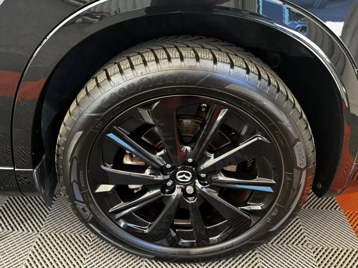 Gros plan sur la roue avant droite noire du Mazda CX-60 2024 avec jante alliage brillante et logo Mazda central.