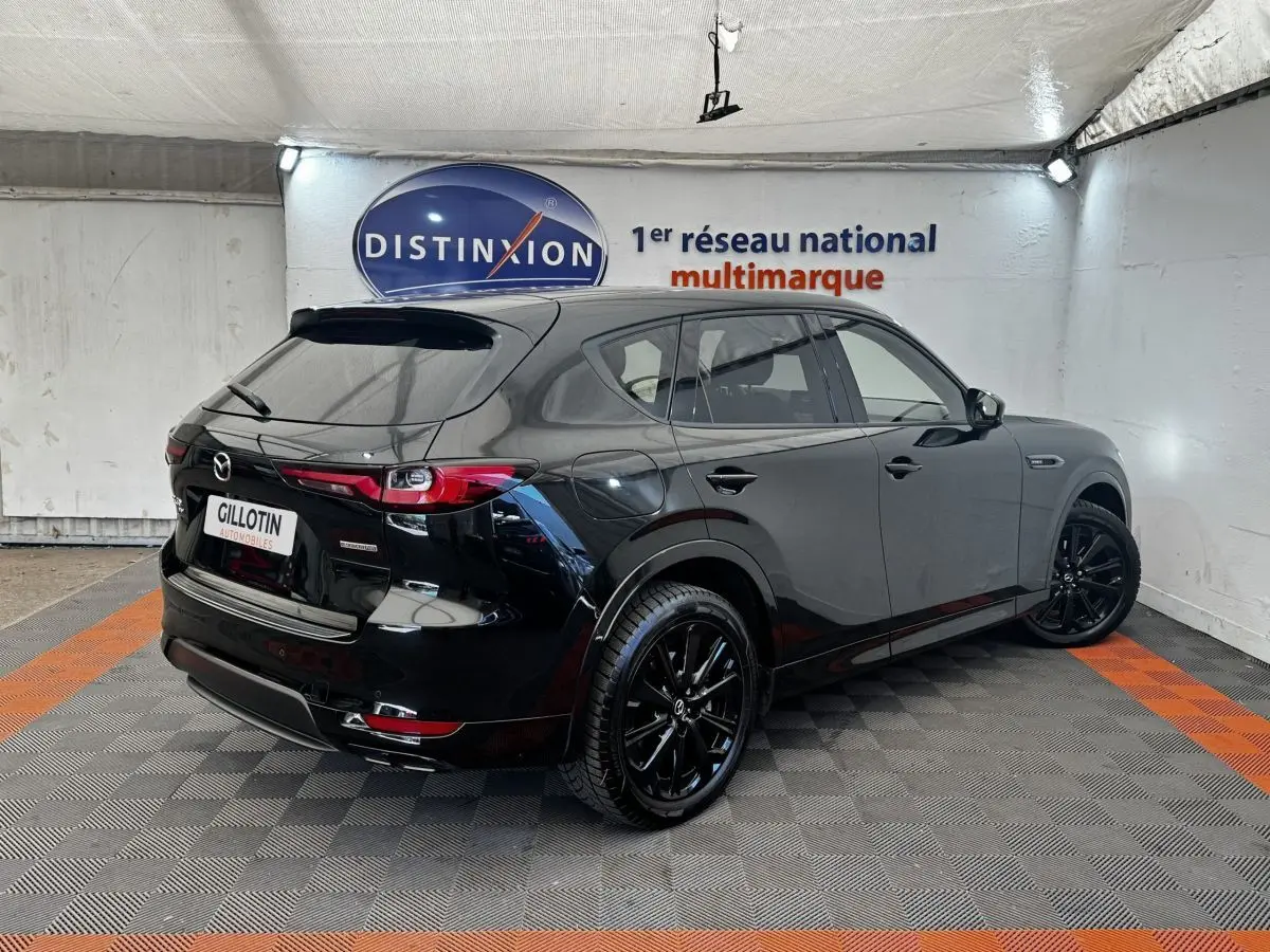 Vue 3/4 arrière droite d'un Mazda CX-60 noir brillant avec jantes noires dans un showroom.