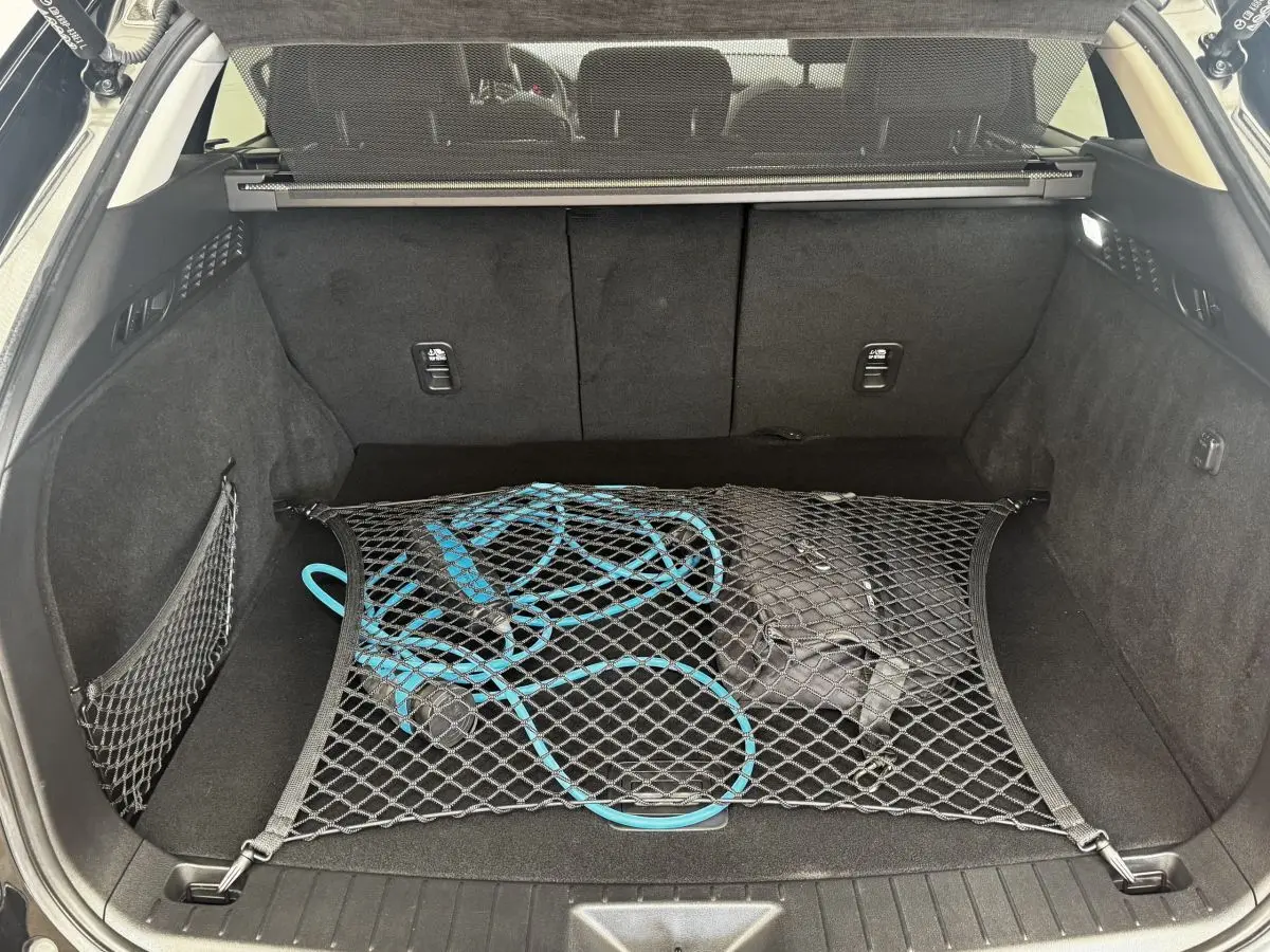 Coffre ouvert vu de l'arrière d'un Mazda CX-60 noir 2024 avec câble de recharge bleu retenu par filet.