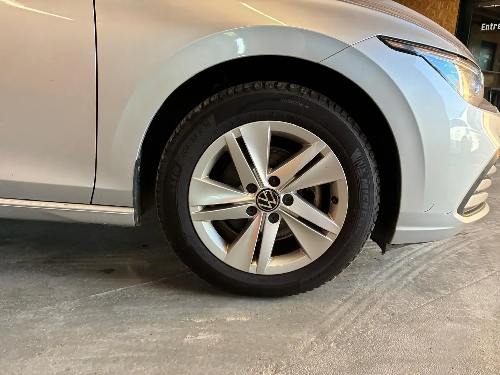 Gros plan sur la roue avant droite d'une Volkswagen Golf gris clair 2023, avec jante alliage et partie avant visible.