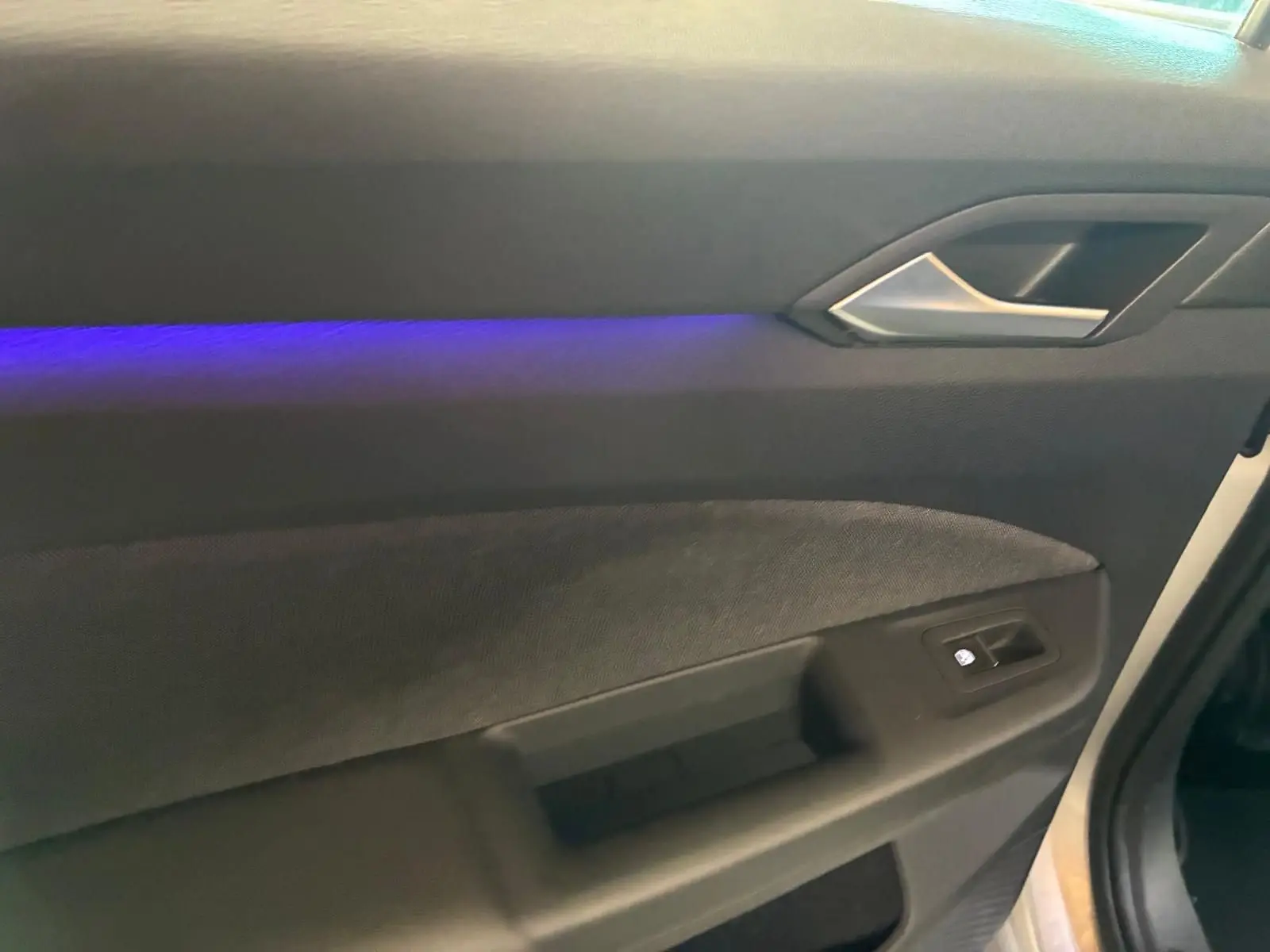 Détail de la porte intérieure côté conducteur de la Volkswagen Golf gris clair 2023 avec éclairage d’ambiance bleu.