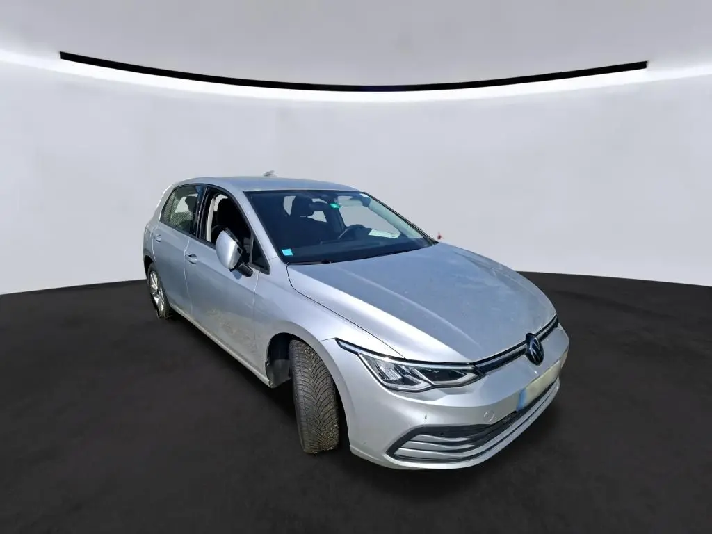 Volkswagen Golf gris clair vue 3/4 avant droit, mettant en valeur ses phares LED et sa calandre épurée.