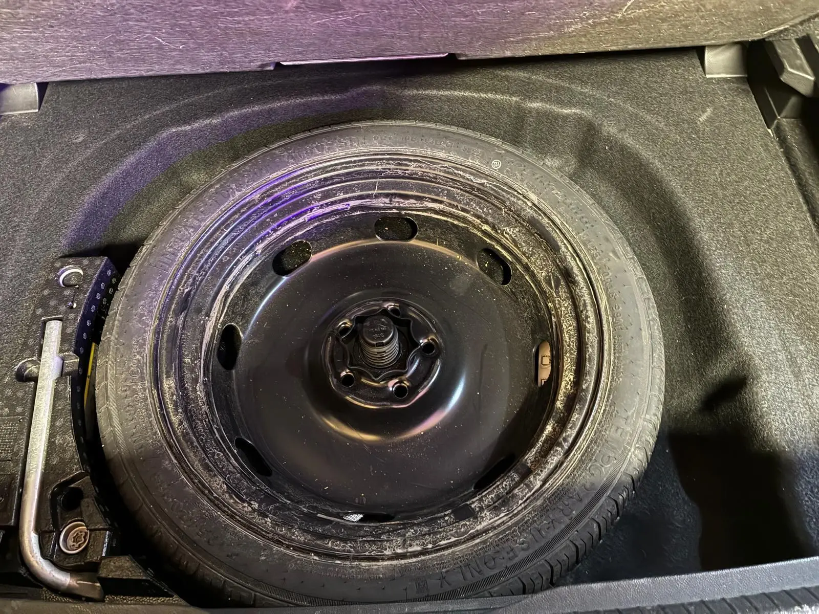 Roue de secours noire dans le coffre d’une Volkswagen Golf 2023 gris clair, vue en plongée sur le pneu et ses outils.