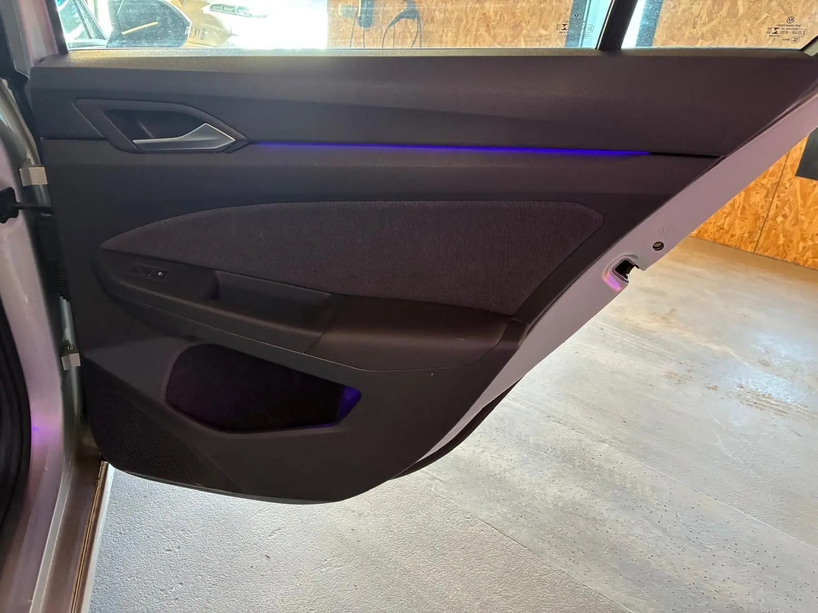 Vue rapprochée de la porte arrière gauche intérieure d’une Volkswagen Golf gris clair 2023 avec éclairage d’ambiance bleu.