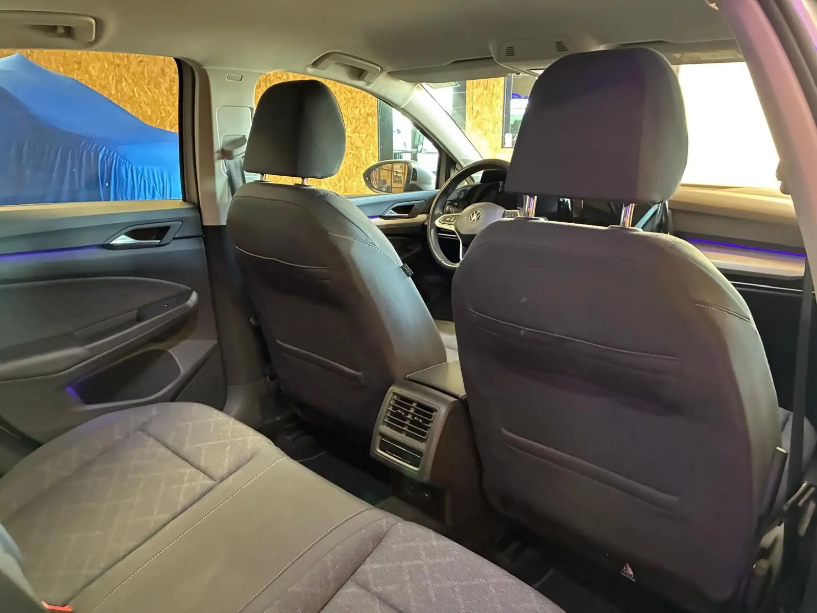 Vue intérieure arrière de la Volkswagen Golf gris clair 2023, montrant les sièges avant et arrière avec éclairage d'ambiance bleu.