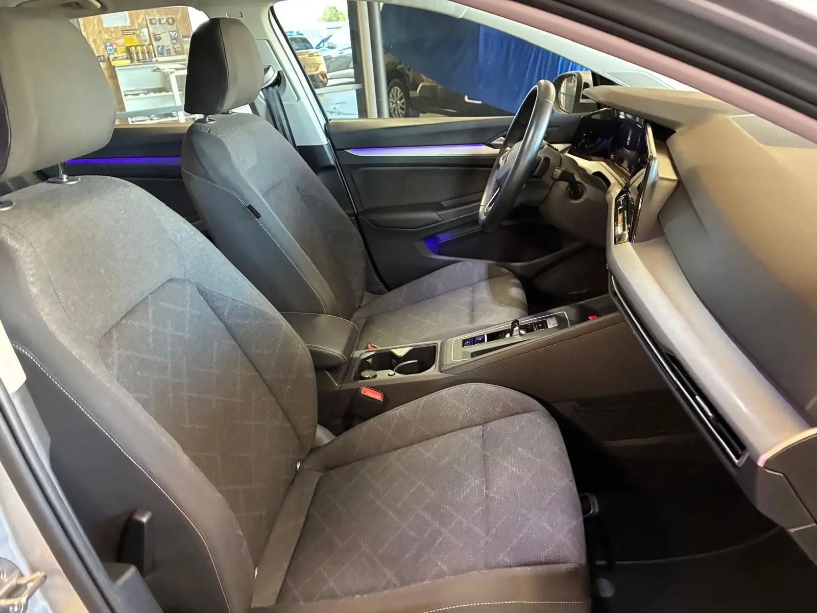 Vue intérieure côté conducteur de la Volkswagen Golf 1.0 eTSI 110 DSG7 Life Plus 2023 avec sièges tissu gris et éclairage d'ambiance violet.