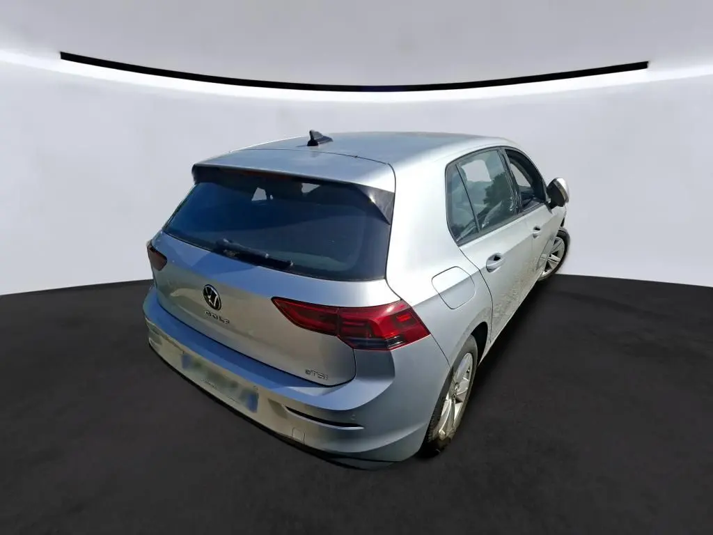 Vue 3/4 arrière droite d'une Volkswagen Golf gris clair 2023, avec feux arrière LED et logo VW visible sur le hayon.