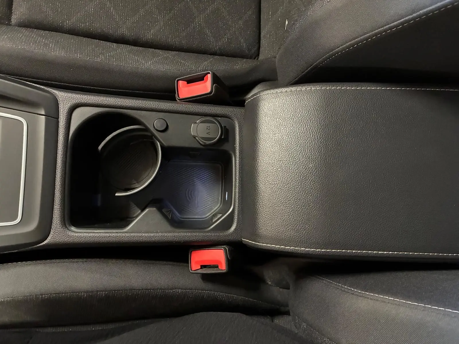 Vue plongeante sur la console centrale noire de la Volkswagen Golf 1.0 eTSI 110 DSG7 Life Plus 2023 avec porte-gobelet et prise 12V.