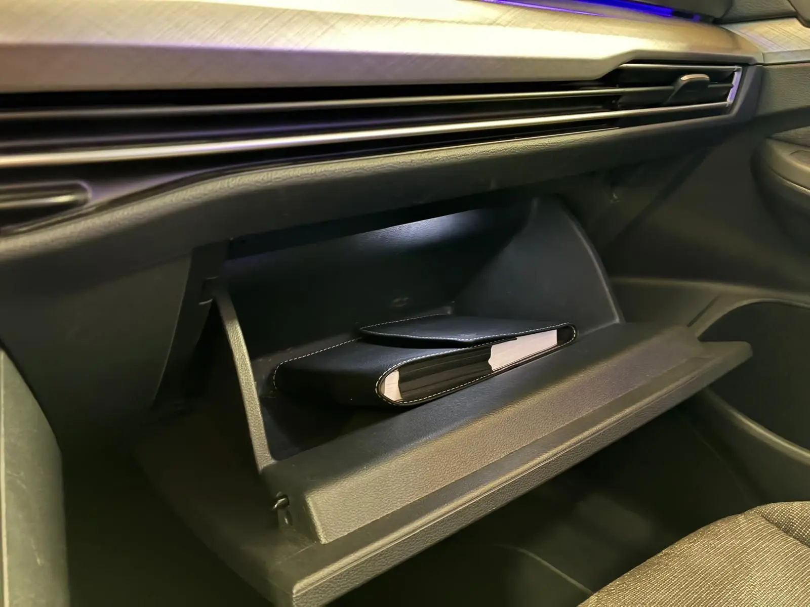 Gros plan sur la boîte à gants ouverte de la Volkswagen Golf gris clair 2023, avec un carnet noir à l'intérieur.