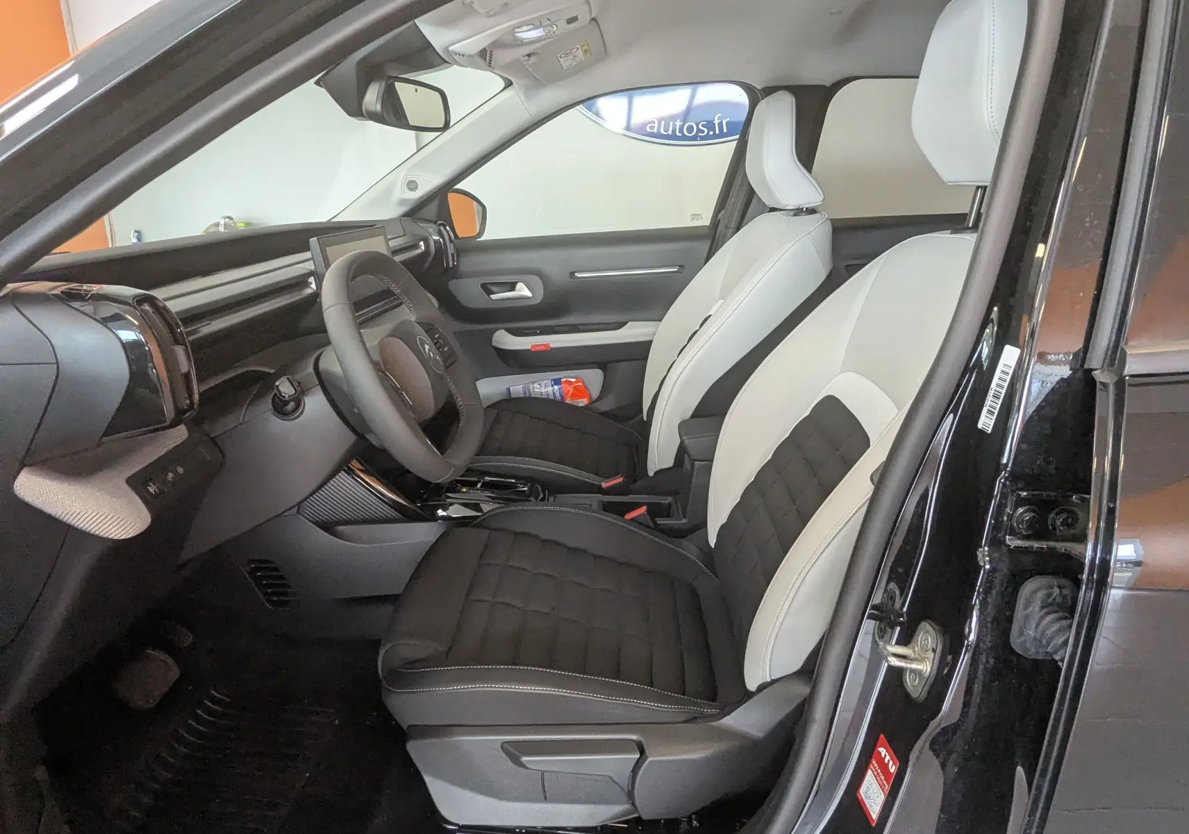 Vue intérieure côté conducteur de la Citroën E-C3 113 MAX 2025 noire, sièges tissu bicolore noir et gris clair.