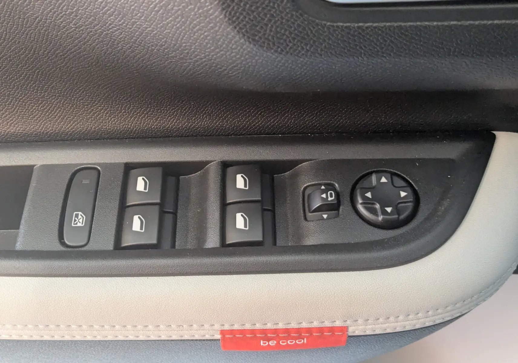 Gros plan sur les commandes de vitres et rétroviseurs côté conducteur de la Citroën E-C3 113 MAX 2025, sellerie gris noir.