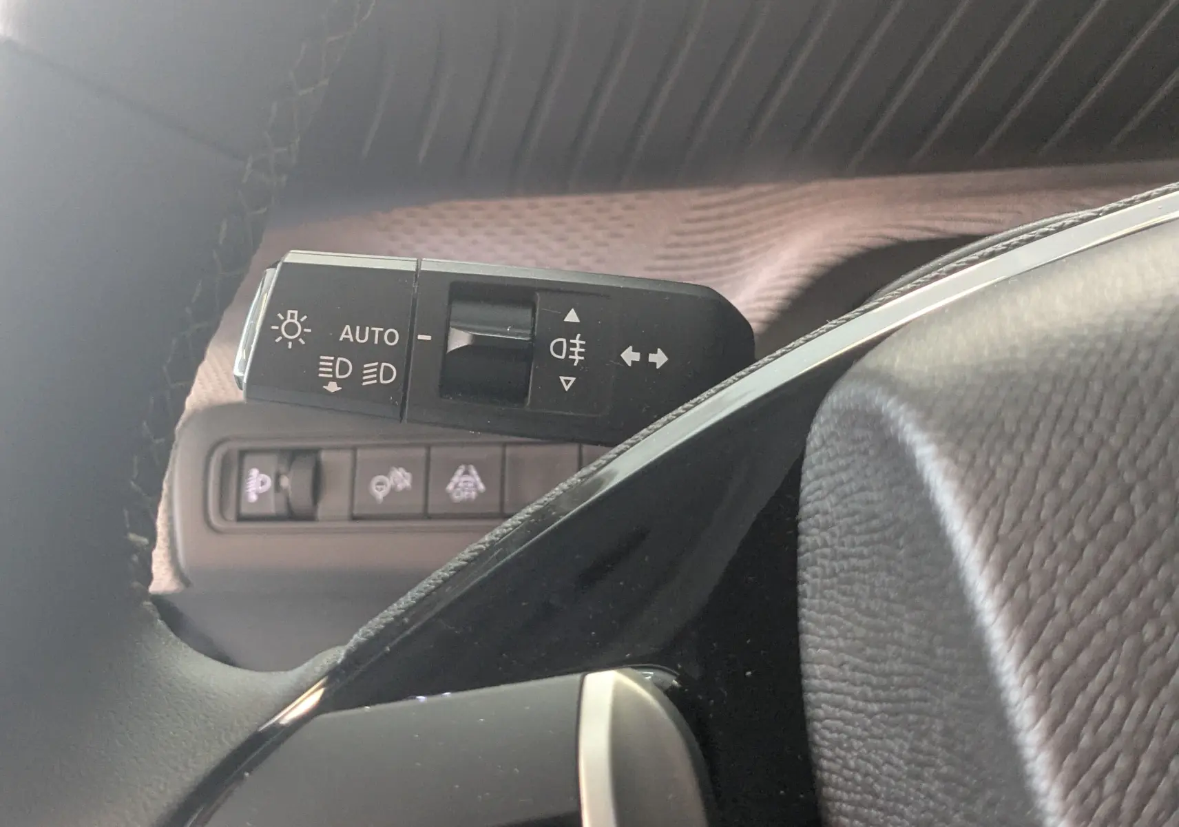 Gros plan sur la commande des feux et clignotants à gauche du volant dans l’habitacle gris noir du Citroën E-C3 2025.