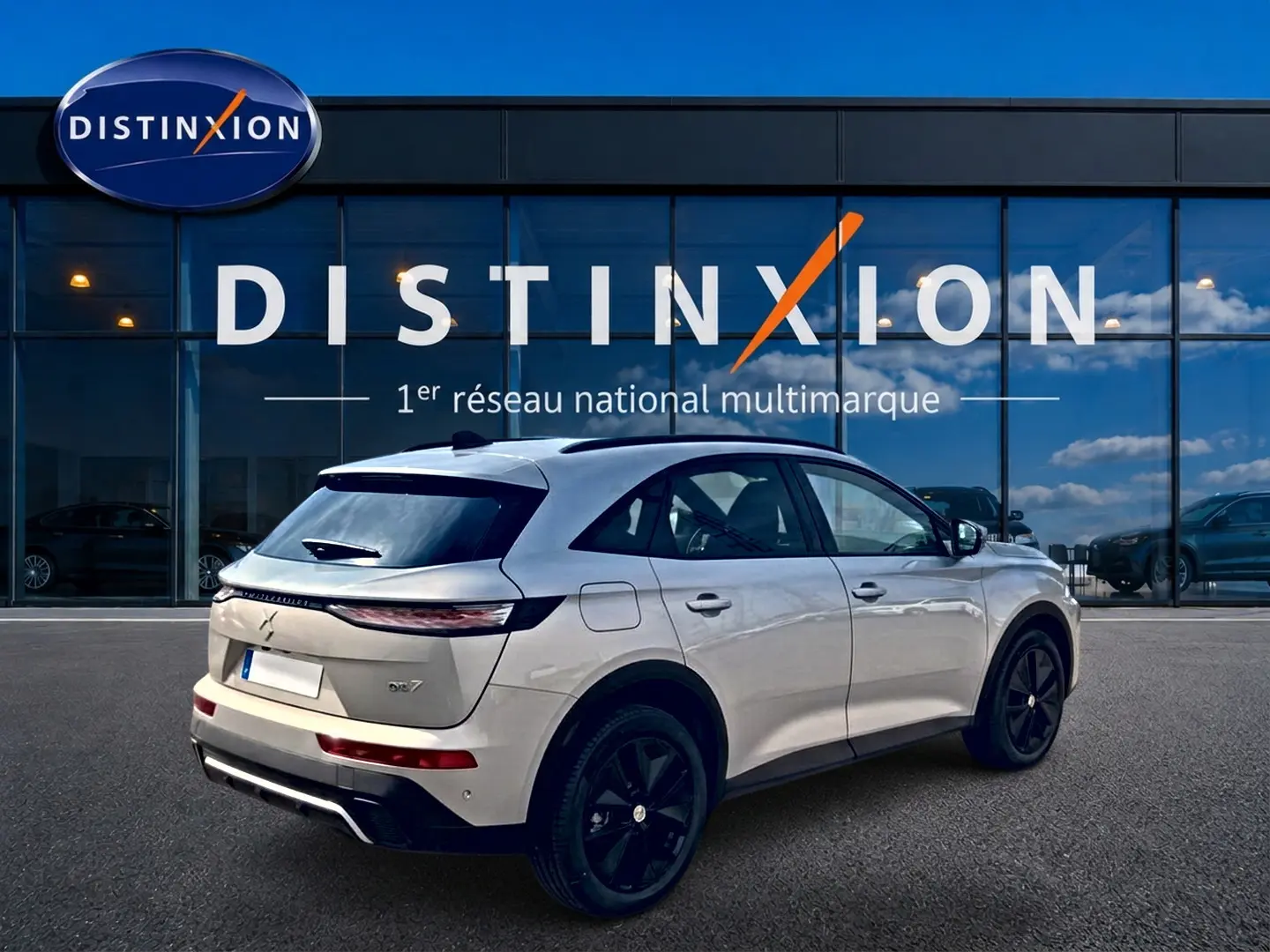 Vue 3/4 arrière droite d'un DS7 Crystal pearl garé devant une vitrine avec logo Distinxion en arrière-plan.
