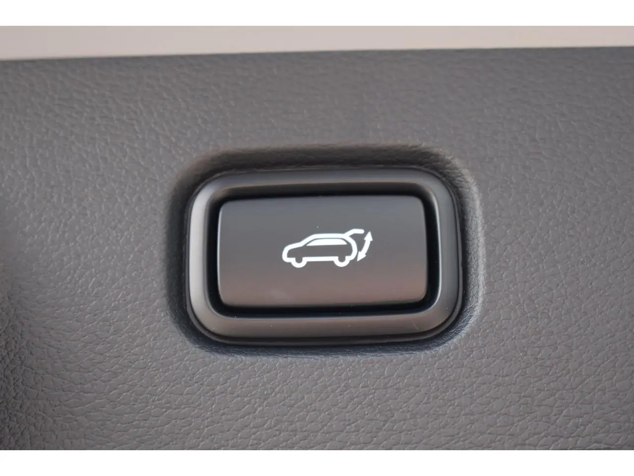 Bouton noir d'ouverture électrique du hayon sur tableau de bord d'un Kia Sportage gris 2026 hybride.