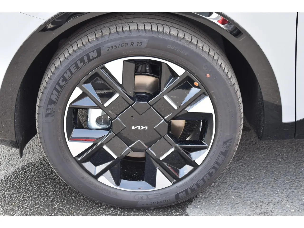 Gros plan sur la jante noire brillante 19 pouces Michelin du Kia Sportage hybride gris, avec logo KIA au centre.