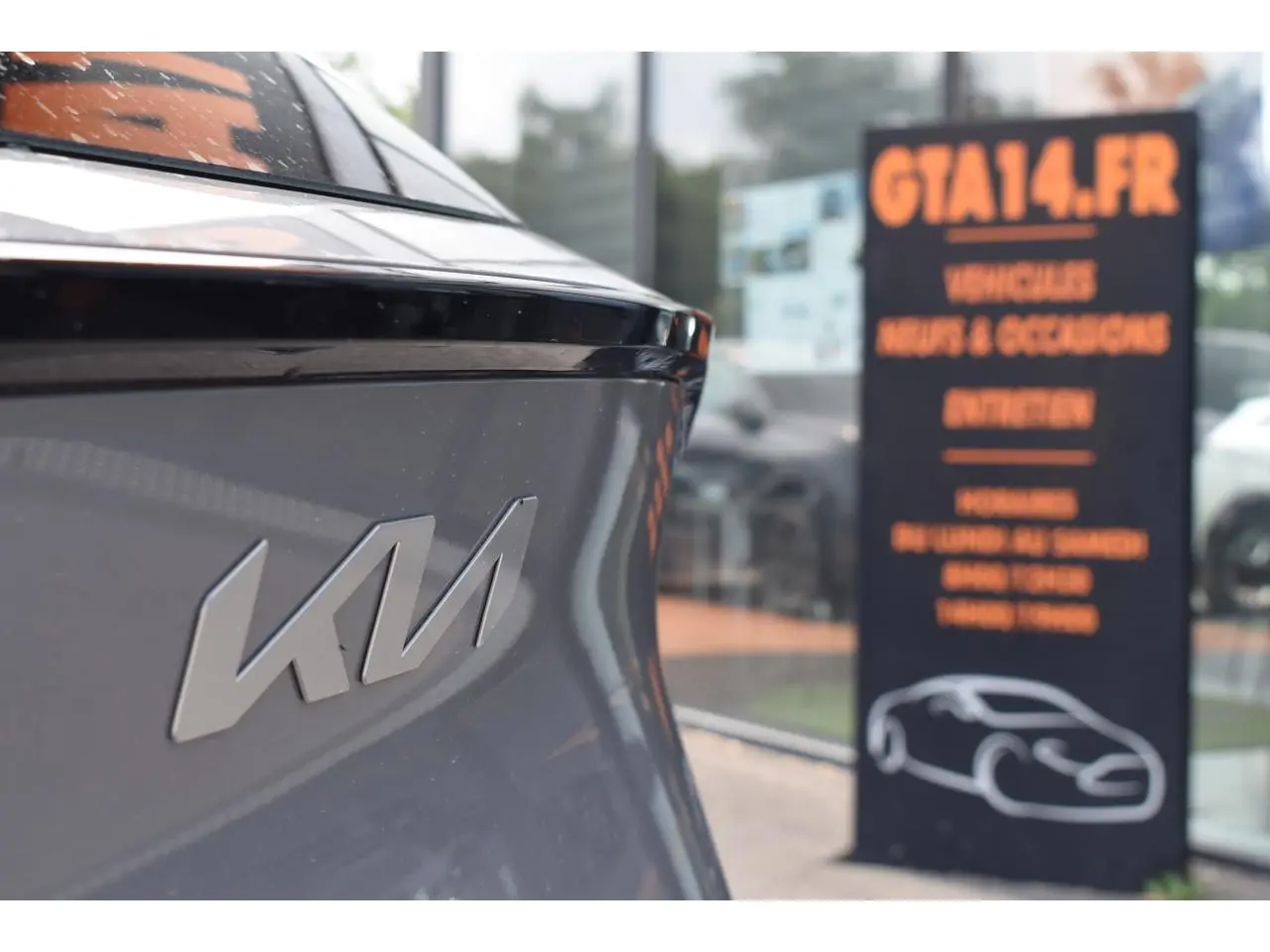 Gros plan sur l'arrière gris du KIA Sportage 2026 avec logo KIA et reflet de vitrine en arrière-plan.