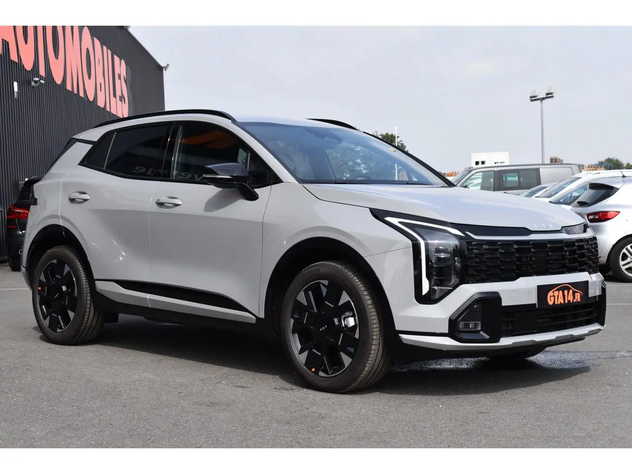 KIA SPORTAGE hybride gris en vue 3/4 avant droit avec jantes noires et calandre imposante.