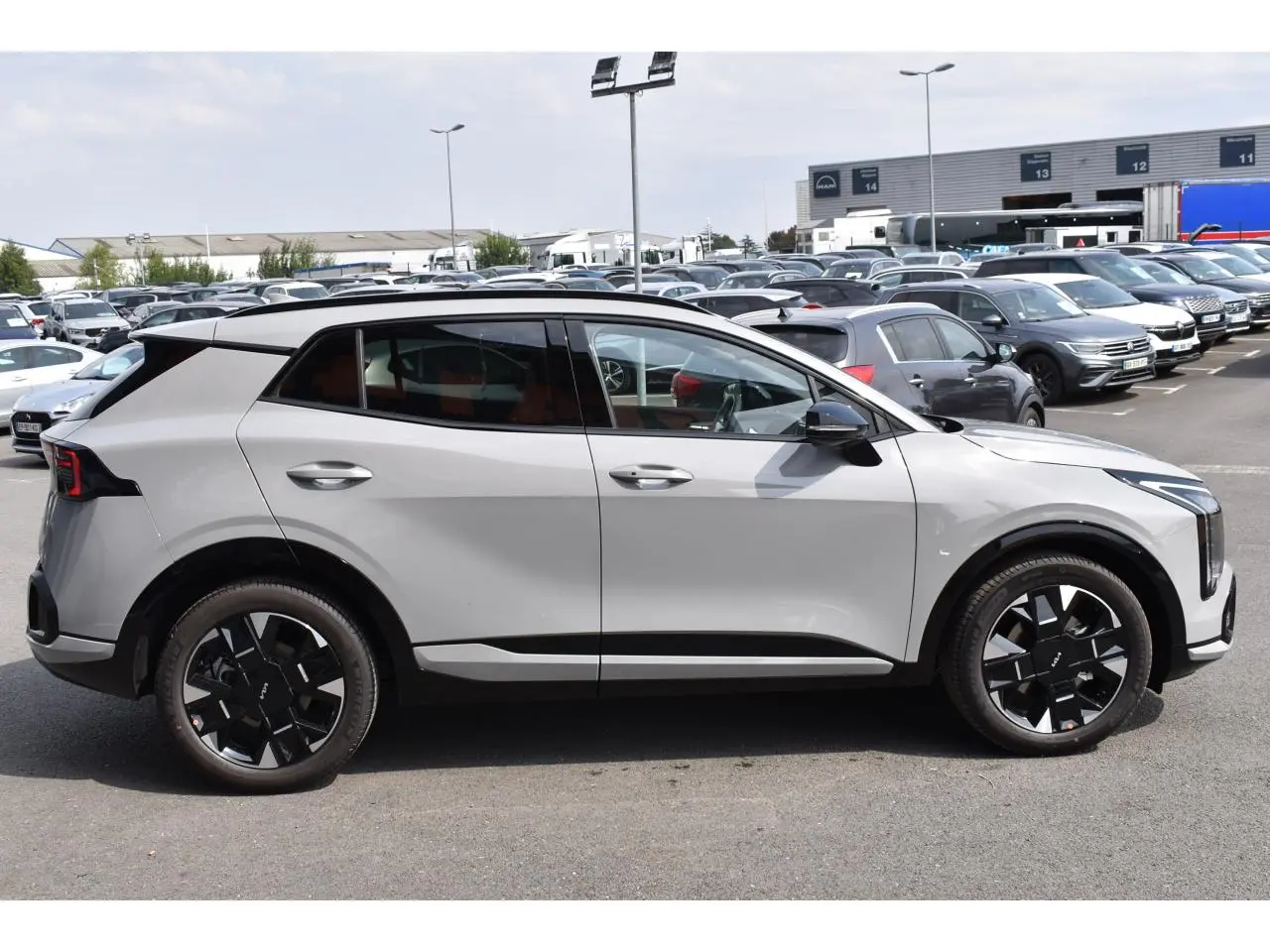 Vue de profil côté gauche du KIA SPORTAGE hybride gris 2026 avec jantes noires distinctives et vitres surteintées.