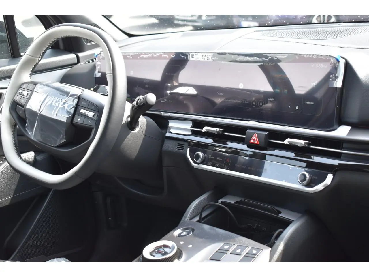 Vue intérieure côté conducteur du tableau de bord du Kia Sportage hybride gris avec écran digital large et volant multifonction.