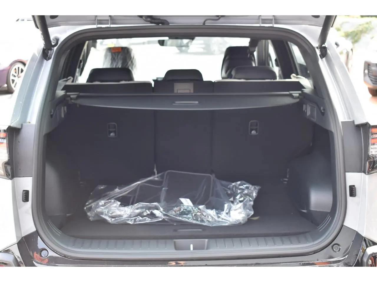 Coffre ouvert vu de l'arrière d'un KIA Sportage gris 2026, montrant l'espace de chargement vide avec cache-bagages.
