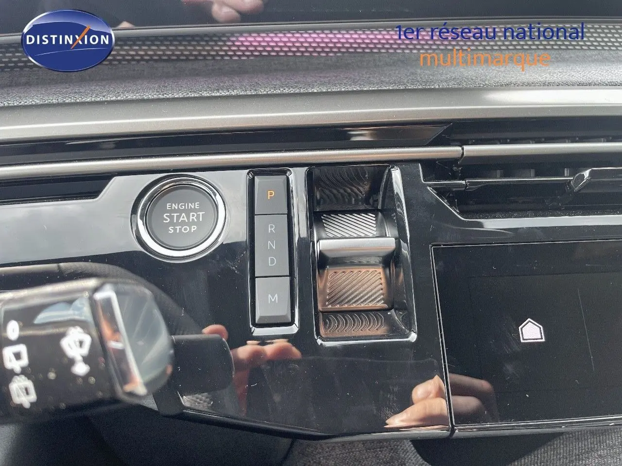 Gros plan sur la console centrale noire brillante du Peugeot 5008 Hybrid 2025 avec bouton start et commandes de boîte automatique.