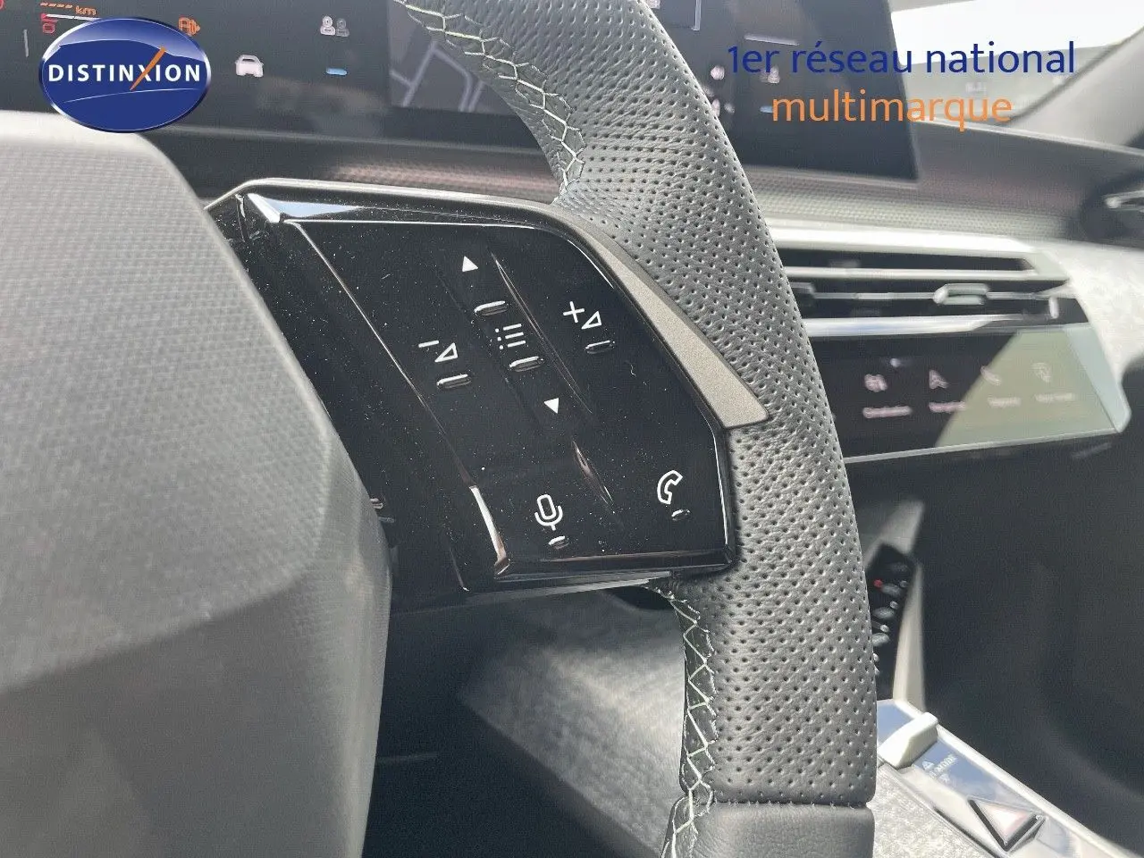 Gros plan sur le volant en cuir perforé noir avec commandes tactiles du Peugeot 5008 Hybrid 2025, tableau de bord en arrière-plan.