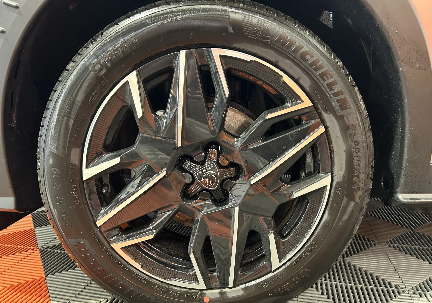 Gros plan sur la jante alliage noire et argentée du Peugeot 3008 gris Artense, avec logo lion central visible.