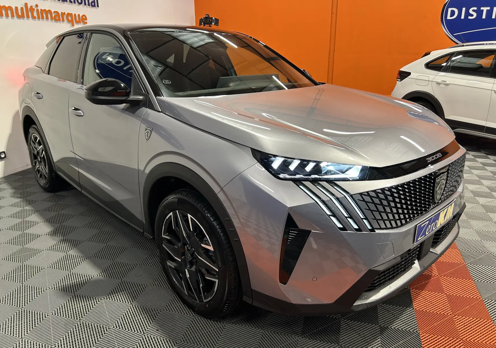 Vue 3/4 avant droite du Peugeot 3008 gris Artense avec phares LED allumés et calandre distinctive en intérieur showroom.