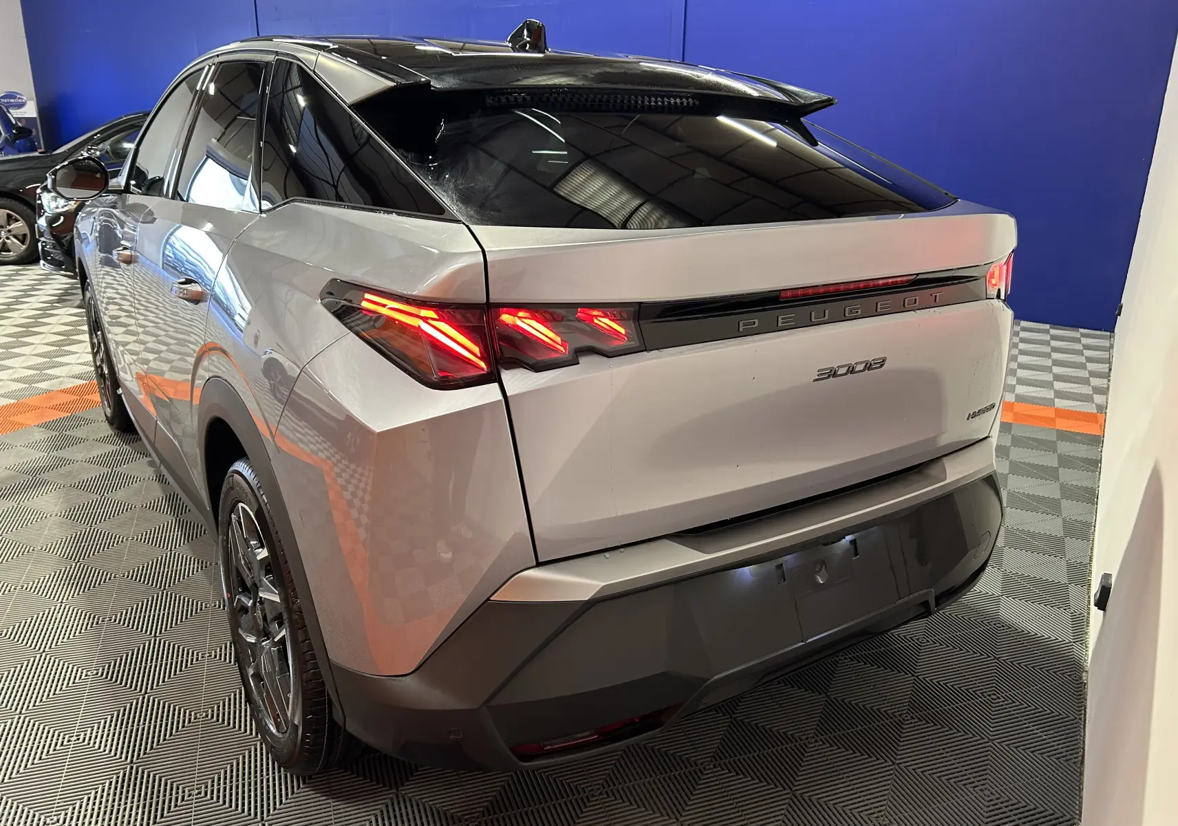 Vue 3/4 arrière droite d’un Peugeot 3008 gris Artense avec feux arrière LED allumés dans un showroom.
