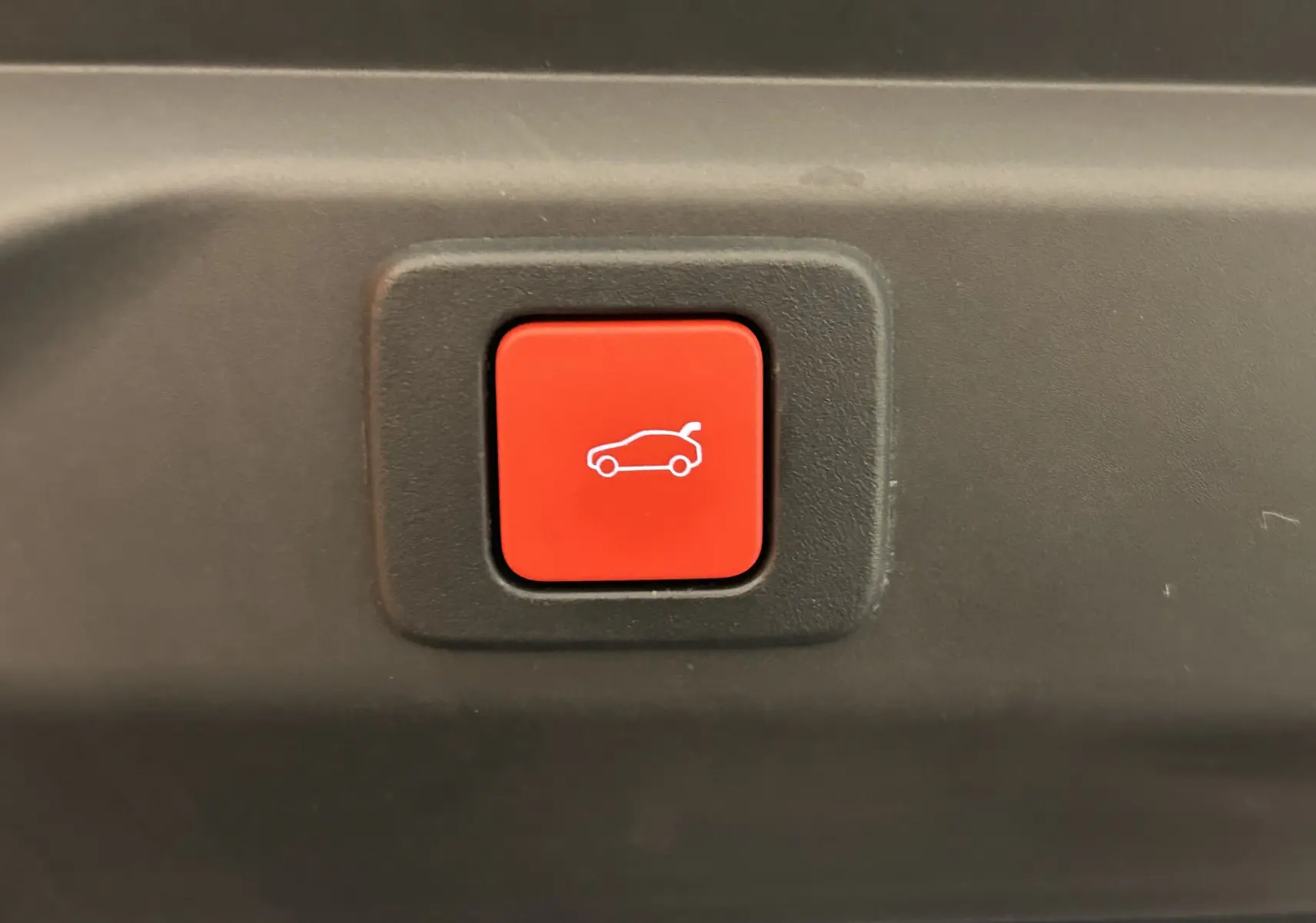 Bouton rouge d'ouverture électrique du hayon sur Peugeot 3008 gris Artense, vue rapprochée intérieure du coffre.