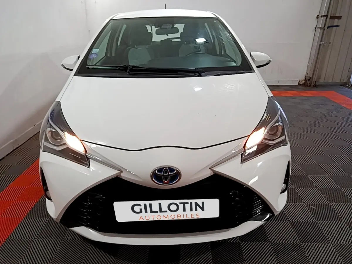 Vue avant d'une Toyota Yaris blanche 2020 avec feux allumés, calandre noire et logo Toyota visible.