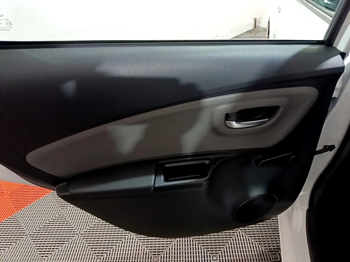 Vue intérieure de la porte arrière droite d'une Toyota Yaris blanche, avec poignée chromée et manivelle de vitre.