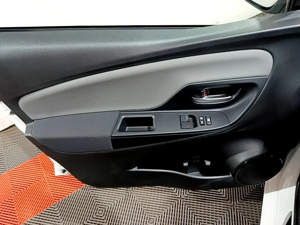 Vue rapprochée de la porte avant gauche de la Toyota Yaris blanche, montrant les commandes des vitres et la poignée intérieure.