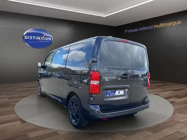 Vue 3/4 arrière droite d’un Citroën Jumpy gris titane avec jantes noires et portes arrière battantes en intérieur showroom.