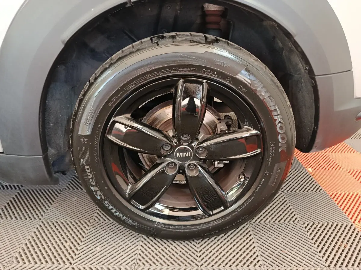 Gros plan sur la roue avant droite d'une MINI Countryman gris foncé avec jante noire brillante à cinq branches.