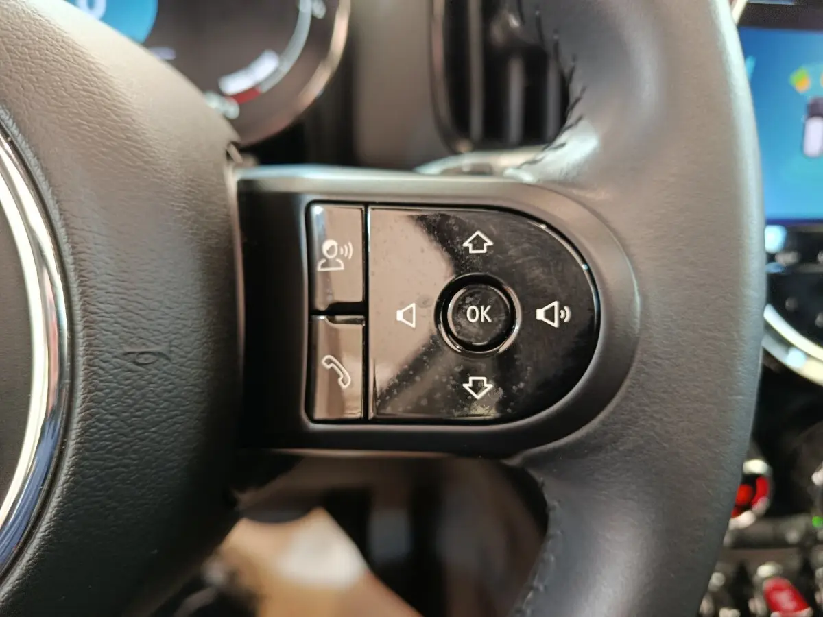Gros plan sur les commandes multifonctions noires du volant cuir d'un MINI Countryman gris foncé, intérieur moderne.