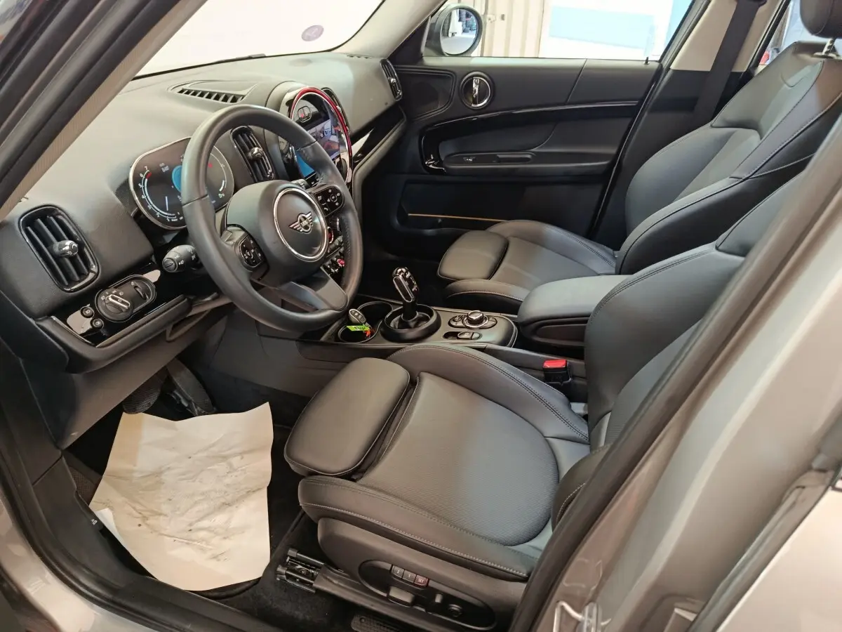 Intérieur avant droit du MINI Countryman gris foncé 2023, avec sièges cuir noirs et tableau de bord digital lumineux.