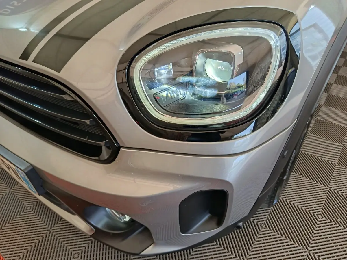 Gros plan sur le phare avant droit et la calandre d’une MINI Countryman gris foncé 2023, finition Cooper Edition Premium Plus.