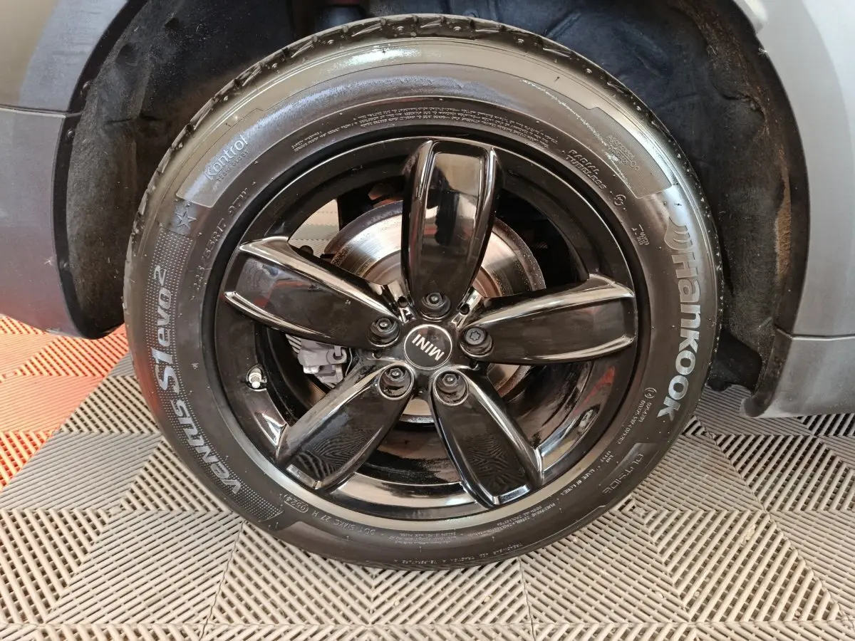 Gros plan sur la roue avant droite noire brillante du MINI Countryman gris foncé, avec jante cinq branches et logo MINI.