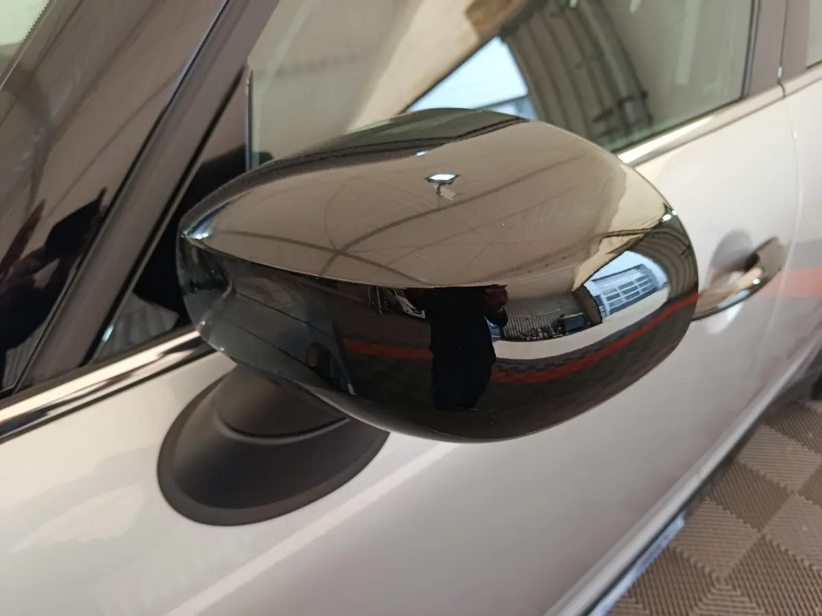 Gros plan sur le rétroviseur noir brillant côté gauche d'un MINI Countryman gris foncé, avec reflet de l'environnement intérieur.