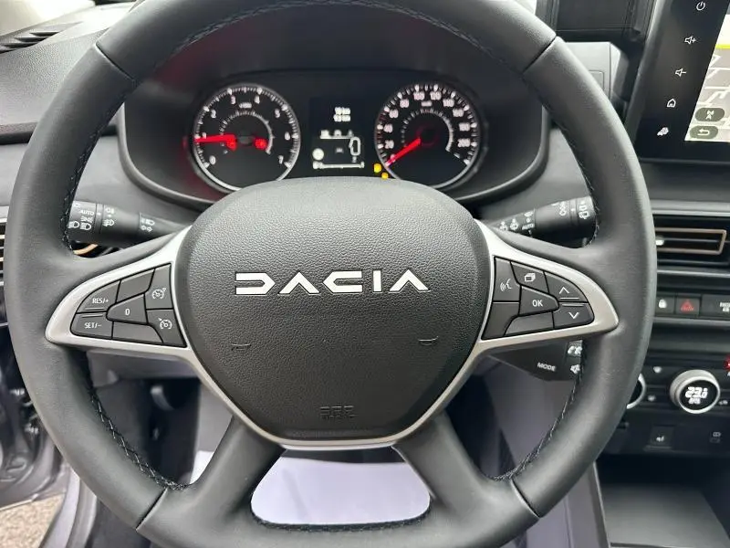 Vue rapprochée du volant noir de la Dacia Jogger 2024, avec commandes intégrées côté droit et tableau de bord visible.