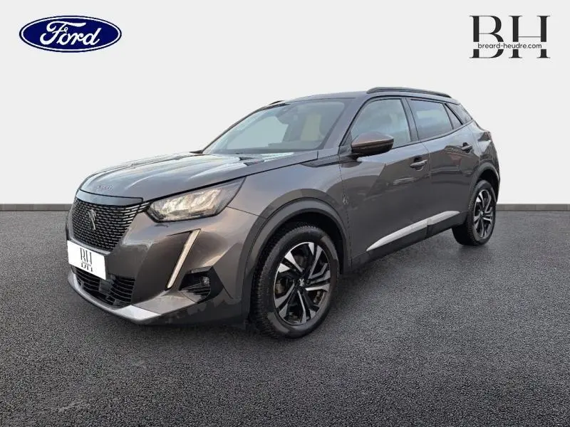 Peugeot 2008 gris Artense vue 3/4 avant droit, avec jantes alu et barres de toit visibles.