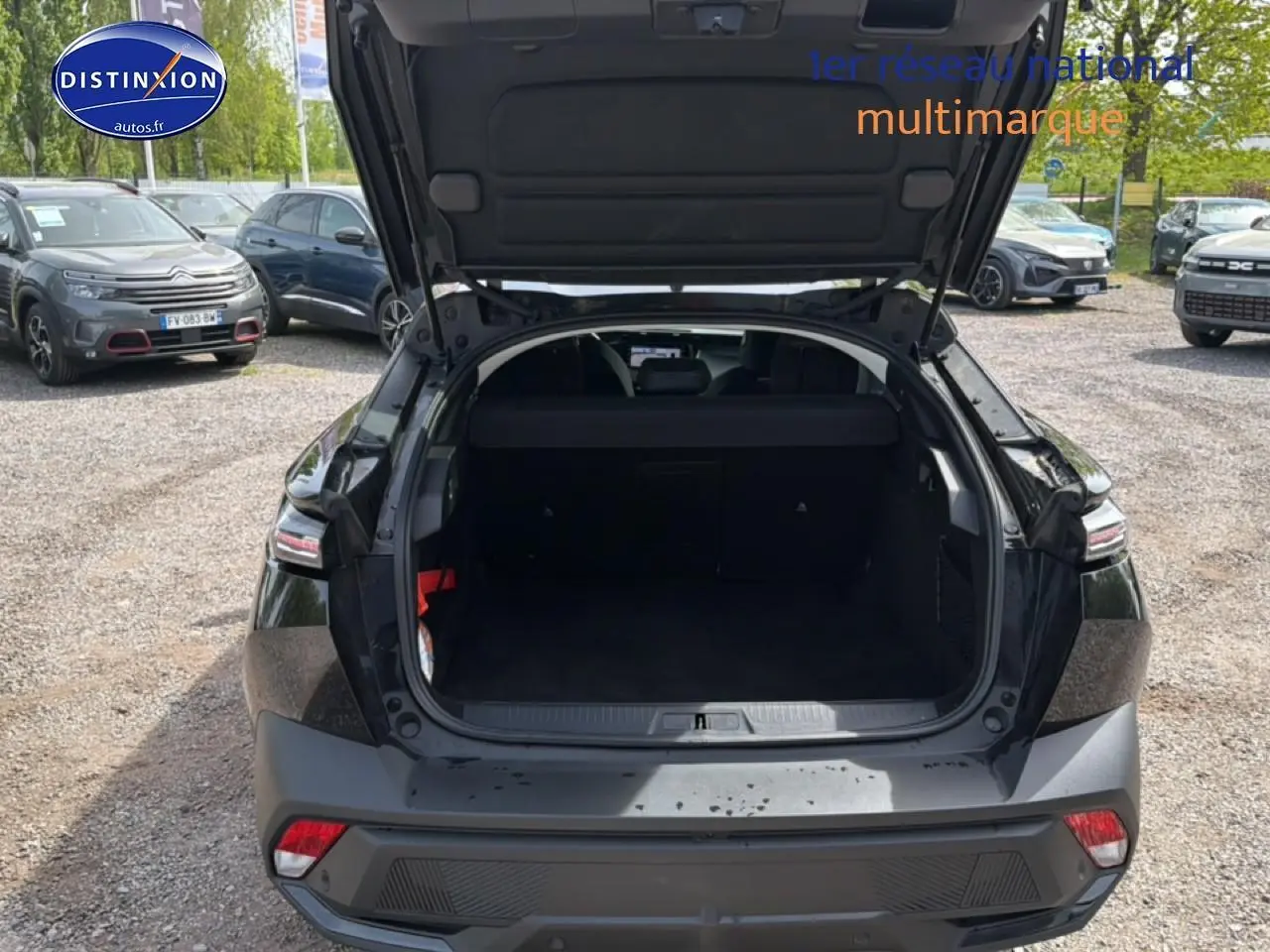 Vue arrière du coffre ouvert d'une Peugeot 408 Hybrid 136 allure e-dcs6 noire, stationnée sur un parking extérieur.