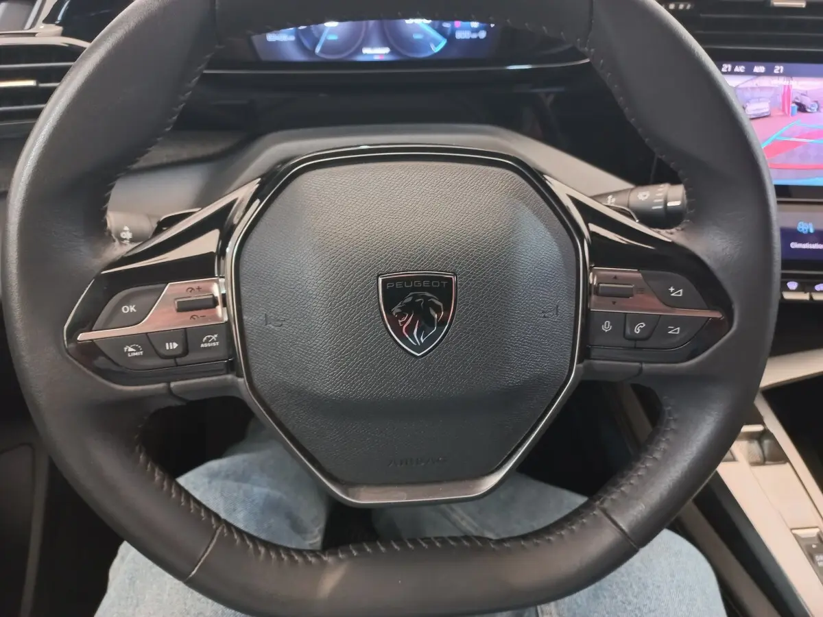 Vue rapprochée du volant cuir multifonctions noir de la Peugeot 308 PureTech 130, avec tableau de bord digital en arrière-plan.