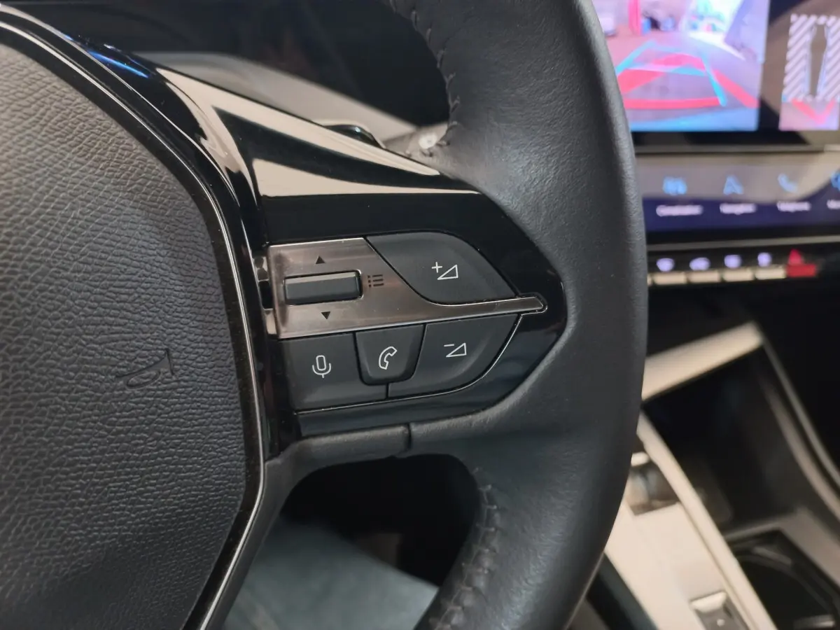 Gros plan sur le volant cuir multifonctions à gauche de la Peugeot 308 bleu, avec commandes audio et vocales visibles.