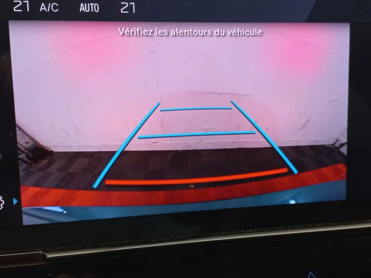 Vue écran caméra de recul d'une Peugeot 308 bleu, avec lignes de guidage bleues et rouges visibles.