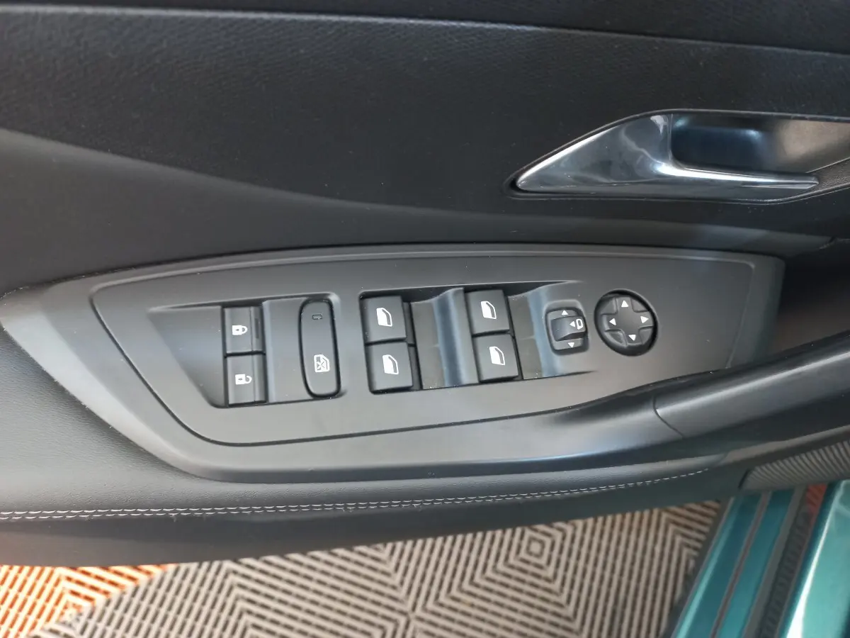 Gros plan sur les commandes de lève-vitres et rétroviseurs sur la porte côté gauche d’une Peugeot 308 bleu.