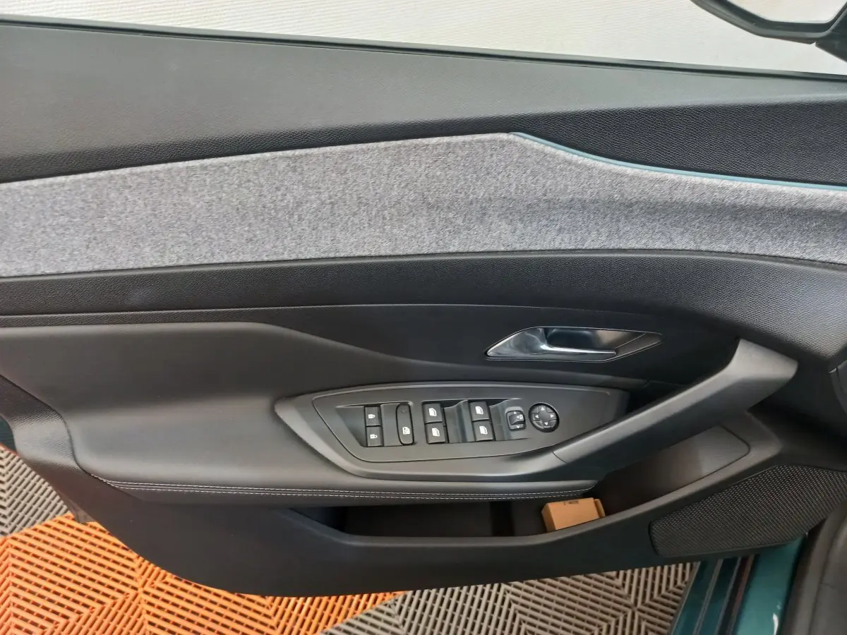 Vue intérieure côté gauche de la porte avant d'une Peugeot 308 bleu, avec commandes électriques des vitres et poignée chrome.